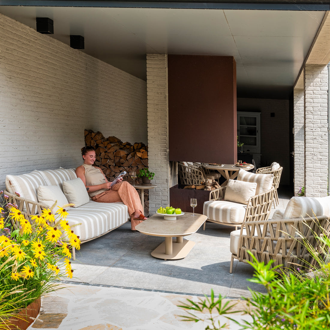 Overbygd terrasse innredet med loungesofa, loungestoler og salongbord ved vedstabel